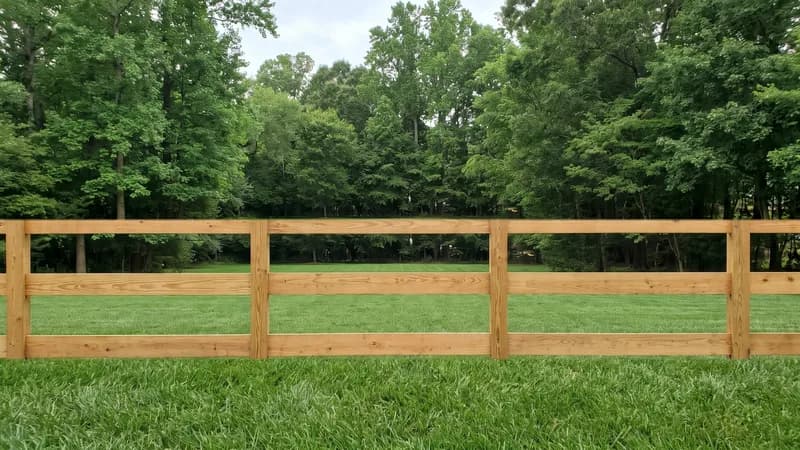 Three-board wooden farm fence running along a green pasture